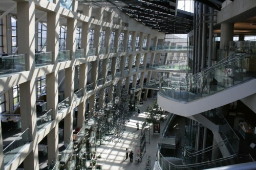 A spacious modern building interior with large windows, glass railings, and artistic installations.