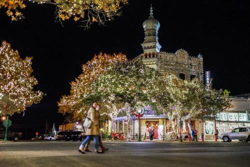 A festive street scene at night, featuring a beautifully lit building and trees adorned with holiday lights.