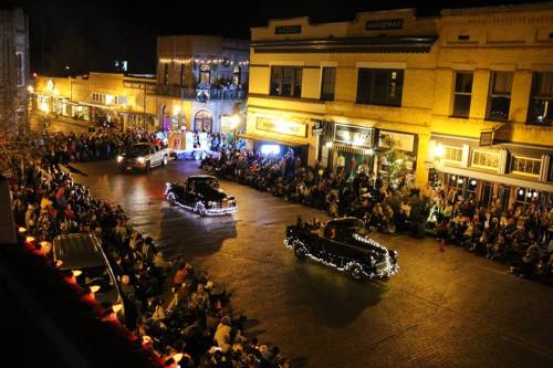 A nighttime parade with decorated cars and a large crowd watching from the streets and buildings.
