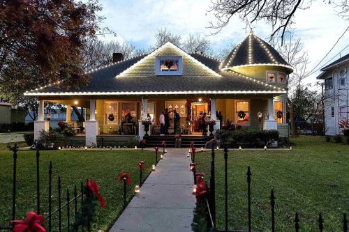 A beautifully decorated house with holiday lights, a festive pathway, and people gathered on the porch.