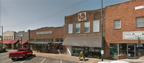 A small-town street featuring brick buildings, shops, and a red pickup truck parked in front.