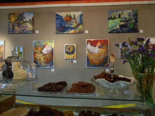 A display of desserts in front of colorful paintings on a gallery wall, with flowers in a vase nearby.