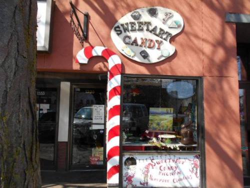A candy shop storefront with a large striped candy cane and colorful displays of sweets in the window.
