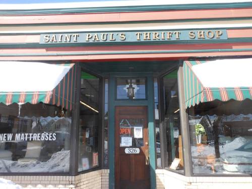 Exterior of Saint Paul's Thrift Shop with a green and red awning, displaying "OPEN" sign and snow outside.
