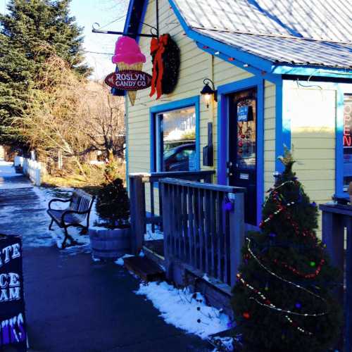 A colorful candy shop with festive decorations, surrounded by snow and benches on a sunny day.