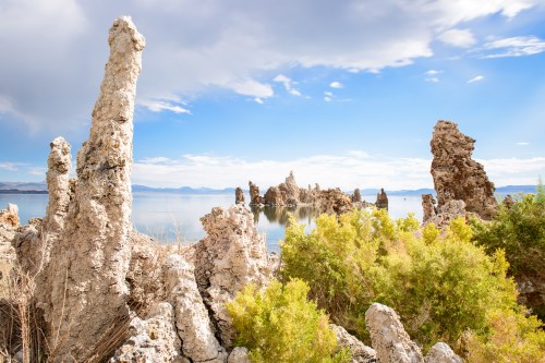 A serene landscape featuring unique rock formations by a calm lake under a blue sky with scattered clouds.