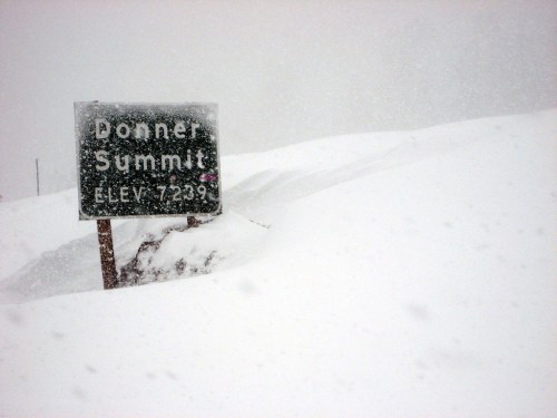 Sign for Donner Summit, elevation 7239 feet, partially buried in deep snow during a snowstorm.