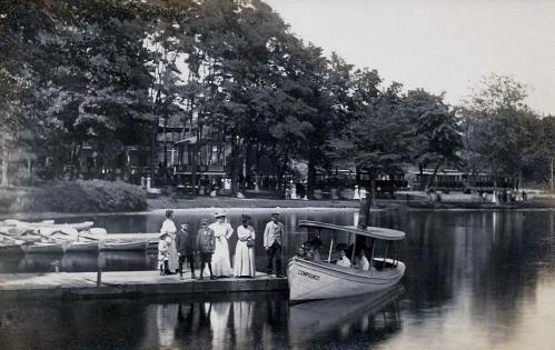 A vintage black-and-white photo of people by a boat dock, with a boat named "Comfort" and trees in the background.