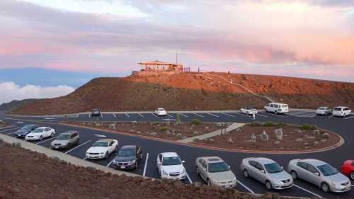 A parking lot with several cars, set against a scenic mountain backdrop and colorful sunset sky.