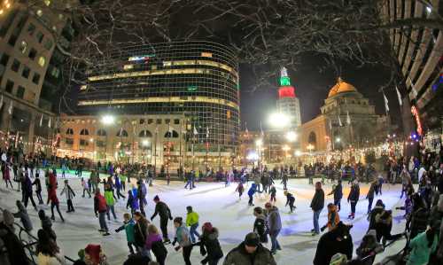 A bustling ice skating rink at night, surrounded by festive lights and tall buildings, with many people enjoying the activity.