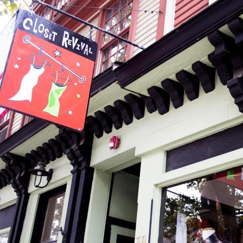 Sign for "Closet Revival" featuring colorful dress silhouettes, hanging on a storefront with decorative trim.