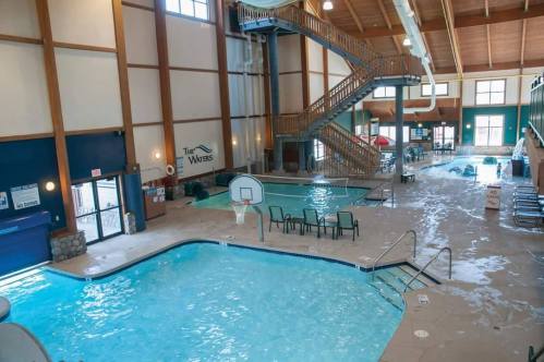 Indoor swimming pool area featuring a large pool, a smaller pool, and a staircase leading to an upper level.