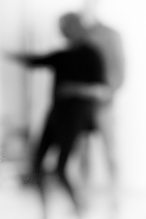 A blurred image of two figures in a dance pose, creating a sense of movement and intimacy.
