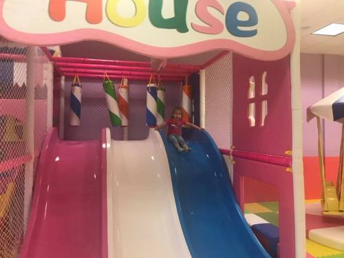 A child slides down a colorful play structure in a bright indoor playground.