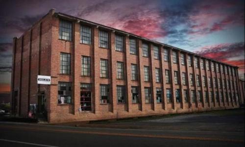 A large brick building with multiple windows, set against a colorful sunset sky.