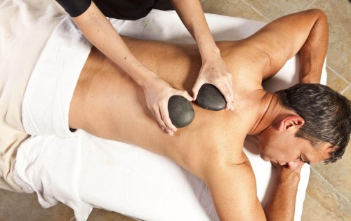 A person receiving a hot stone massage on their back, with two smooth stones placed on their skin.