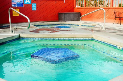 A view of a hot tub with a blue tile design, surrounded by a pool area and red wooden walls.