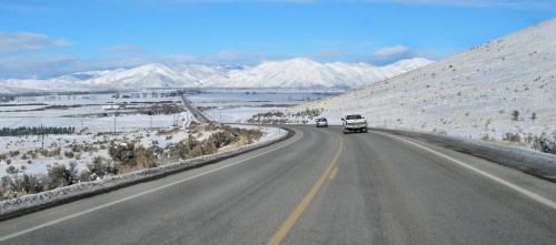 A winding road through a snowy landscape with mountains in the background under a clear blue sky.