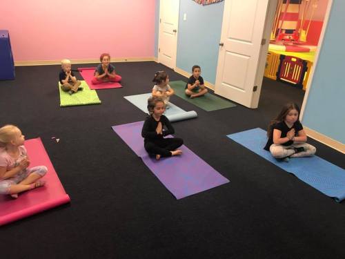 A group of children practicing yoga on colorful mats in a bright, playful room.