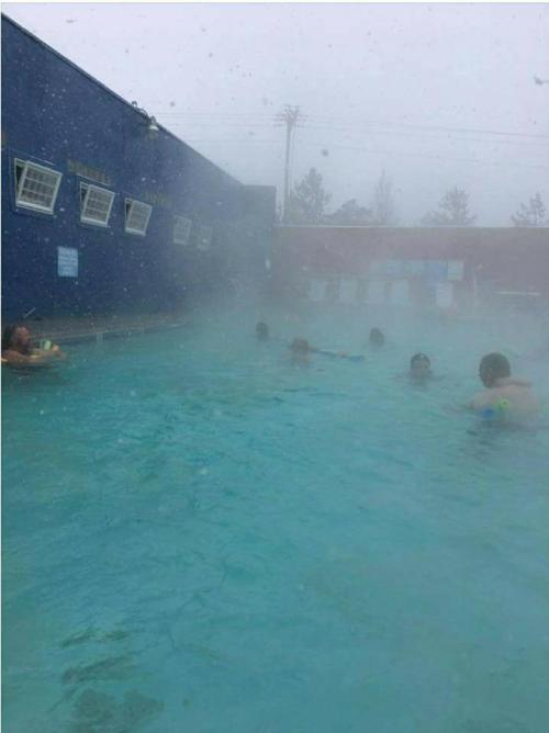A misty pool scene with people swimming, surrounded by fog and a blue building in the background.