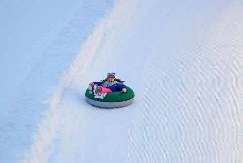 A child joyfully sledding down a snowy slope on a green inner tube.