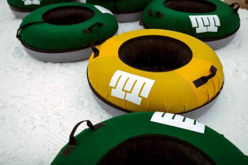 Colorful snow tubes in green and yellow, resting on a snowy surface, ready for winter fun.