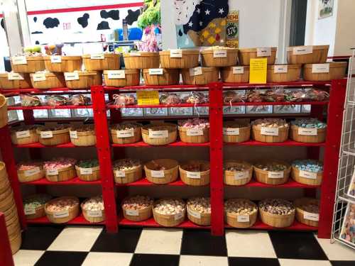 A colorful display of baskets filled with various candies on red shelves in a shop. Black and white checkered floor visible.