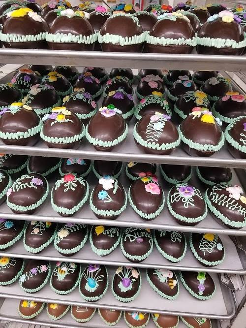 A display of chocolate-covered pastries decorated with colorful icing flowers on multiple shelves.