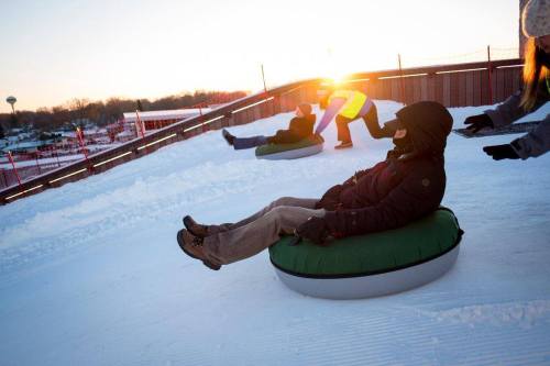 People enjoying snow tubing on a snowy slope at sunset, with colorful tubing lanes in the background.