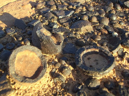 Close-up of various black, rounded rock formations scattered on a sandy surface.
