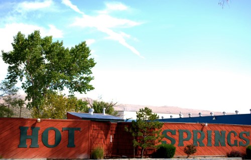 A red building with "HOT SPRINGS" painted on the side, surrounded by trees and a clear blue sky.