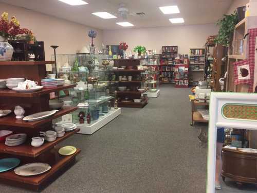 A spacious thrift store aisle filled with shelves of dishes, glassware, and home decor items.