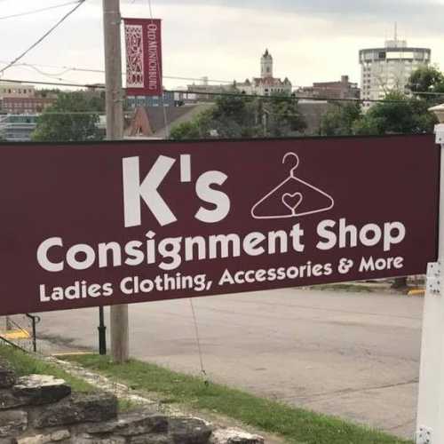 Sign for K's Consignment Shop, featuring ladies' clothing, accessories, and more, with a cityscape in the background.