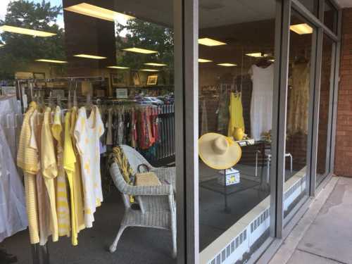 A storefront display featuring yellow clothing and accessories, including dresses, hats, and a wicker chair.