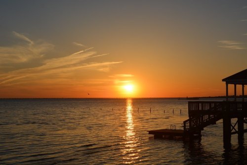 A serene sunset over calm waters, with a silhouette of a dock and gentle clouds in the sky.