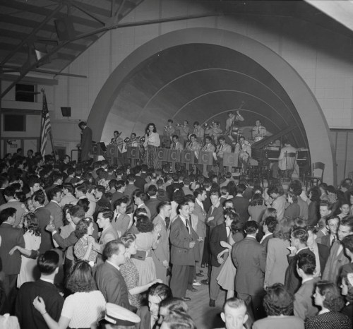 A lively dance hall scene with a big band performing on stage and couples dancing in the foreground.