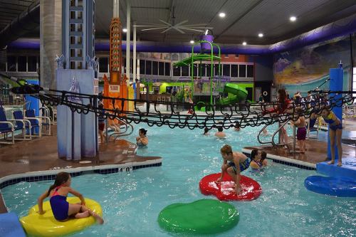 A vibrant indoor water park with slides, a lazy river, and children playing on colorful floaties in the pool.