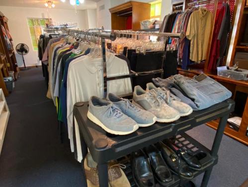 A clothing rack with various shirts and pants, alongside a cart of shoes and accessories in a store setting.