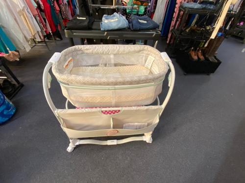 A baby bassinet on display in a store, featuring a soft fabric and storage pockets underneath.