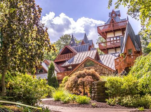 A unique, multi-level house with a mix of architectural styles, surrounded by lush greenery and bright blue skies.