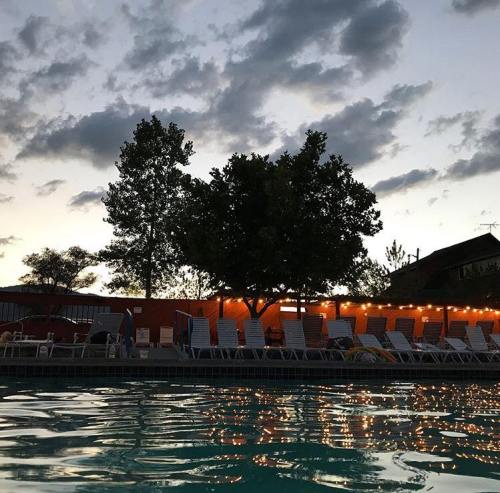 A serene poolside scene at dusk, with lounge chairs, trees, and twinkling lights against a cloudy sky.