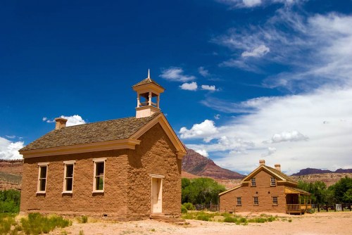 Two historic adobe buildings under a bright blue sky with scattered clouds, surrounded by desert landscape.