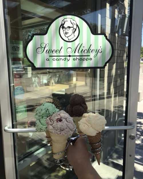 A hand holding five ice cream cones in front of a candy shop entrance with a sign that reads "Sweet Mickey's."