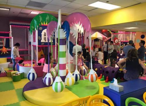 A colorful indoor play area filled with children playing, climbing structures, and parents supervising in a vibrant setting.