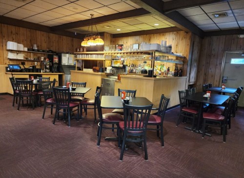 Cozy restaurant interior with wooden walls, a bar area, and several tables set for dining.