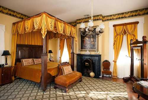 A vintage bedroom featuring a four-poster bed, ornate curtains, a fireplace, and elegant decor in warm tones.