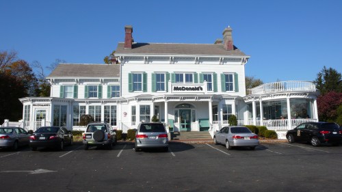 A McDonald's restaurant in a large, historic house with a parking lot filled with cars. Clear blue sky above.