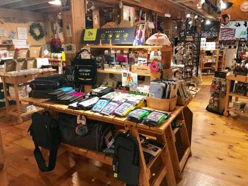 A wooden display table filled with various products in a cozy, rustic store. Shelves are stocked with items in the background.