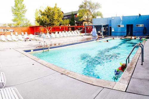 A sunny outdoor pool area with lounge chairs, trees, and people swimming in the water.