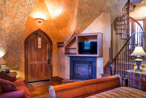 Cozy room with a wooden door, fireplace, TV, and spiral staircase, featuring warm, textured walls and soft lighting.
